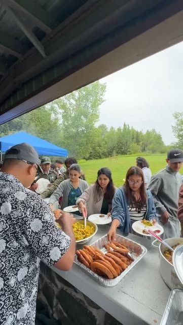 Volunteers serving food from a long table under a shelter at the community picnic.